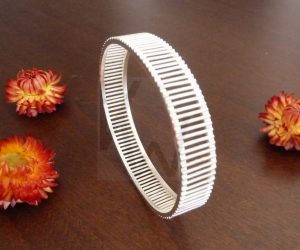 Brazalete artesanal de Plata de Ley 925 formado por dos aros paralelos de perfil cuadrado, conectados entre sí por una sucesión de múltiples varillas verticales; el diseño crea un efecto de galería abierta que permite el paso de la luz a través de su estructura geométrica.