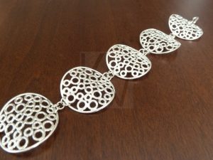 Pulsera artesanal de plata formada por cinco eslabones circulares articulados entre sí; cada elemento presenta un diseño calado compuesto por numerosos aros pequeños de Plata de Ley 925 y posee una curvatura anatómica diseñada para adaptarse cómodamente a la forma del brazo.
