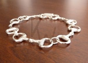 Pulsera artesanal de plata compuesta por cinco motivos de filete ecuestre articulados y dispuestos en fila; el diseño destaca por su movimiento fluido y su acabado pulido en Plata de Ley 925, que rinde tributo a la tradición hípica con un estilo refinado.