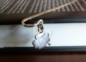 Marcapágina artesanal realizado en Plata de Ley 925 con terminación pulida de alto brillo; la pieza presenta una terminal diseñada para sobresalir del libro, de la cual suspende un trébol de cuatro hojas detallado mediante una pequeña asa. Ofrece la posibilidad de personalizar el diseño con el grabado de iniciales, convirtiéndolo en un objeto de uso personal único y sofisticado.