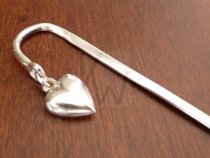 Marcapágina artesanal de plata diseñado para quedar integrado entre las páginas, del cual pende un pequeño corazón de Plata de Ley 925; el motivo queda suspendido delicadamente por fuera del libro, marcando el punto de lectura con un detalle elegante y lleno de sentimiento.