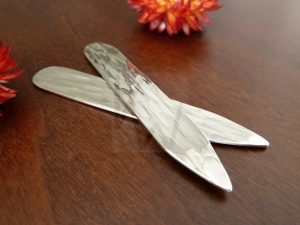 Pareja de ballenas de camisa artesanales realizadas en Plata de Ley 925 con un acabado martillado y pulido; cada pieza, de 4 cm de largo por 1 cm de ancho, presenta una superficie facetada que evoca el movimiento del agua. Un accesorio de sastrería exclusivo que ofrece la posibilidad de personalizar sus medidas para adaptarse perfectamente a cualquier tipo de cuello de camisa.