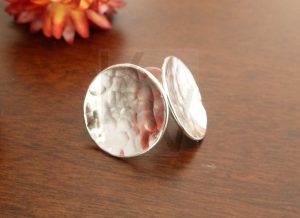 Pendientes artesanales de plata con forma circular y superficie martillada; el acabado manual crea sutiles facetas que capturan la luz de forma irregular, imitando el movimiento y los destellos del agua sobre la Plata de Ley 925.