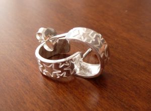 Pareja de pendientes artesanales realizados en Plata de Ley 925 con un acabado pulido de alto brillo; cada pieza se crea a partir de un rectángulo con un delicado estampado de múltiples estrellas, el cual ha sido curvado para formar un aro elegante que permite que el motivo estelar recorra toda la silueta del pendiente.