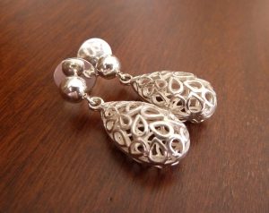 Pendientes artesanales de plata con diseño calado compuesto por múltiples gotas pequeñas que se agrupan para formar una silueta de gota mayor; la pieza se encuentra suspendida de una pequeña esfera de Plata de Ley 925 que sirve de base.