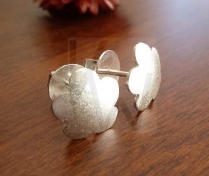 Pendientes artesanales de plata con diseño de flor de cinco pétalos; presentan una forma abombada que aporta volumen y un acabado satinado que ofrece un brillo suave y aterciopelado sobre la Plata de Ley 925.