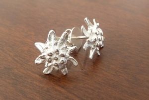 Pareja de pendientes artesanales realizados en Plata de Ley 925, cada uno con la forma de una flor Edelweiss; el diseño recrea con precisión los pétalos aterciopelados y la estructura característica de esta flor alpina, ofreciendo una pieza delicada y atemporal que celebra la naturaleza de alta montaña.