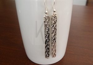 Pareja de pendientes artesanales realizados en Plata de Ley 925 con terminación pulida de alto brillo; cada pieza presenta una pequeña esfera que se posiciona en el lóbulo, de la cual suspende un rectángulo con iniciales estampadas de forma personalizada. Un diseño que une equilibrio y exclusividad, permitiendo que la identidad propia luzca con un brillo constante.