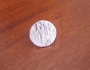 Marcapelotas de golf artesanal realizado en Plata de Ley 925; la superficie presenta un minucioso trabajo de martillado que recrea la textura rugosa de la corteza de un árbol, ofreciendo un diseño orgánico que resalta bajo la luz natural del campo de juego.