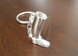 Llavero artesanal realizado en Plata de Ley 925 con una terminación pulida de alto brillo; se compone de un aro principal del que parte una cadena que sostiene una figura detallada de una bota de montar a caballo, logrando un diseño elegante que rinde homenaje a la tradición ecuestre.
