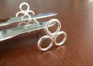 Apoyacuchillo artesanal realizado en Plata de Ley 925 con terminación pulida de alto brillo; el diseño se compone de una barra central que se ensambla en sus extremos al núcleo de unión de tres aros. Esta estructura geométrica no solo aporta una estética vanguardista y simétrica, sino que eleva la cubertería con elegancia sobre la mesa, capturando la luz desde múltiples ángulos.