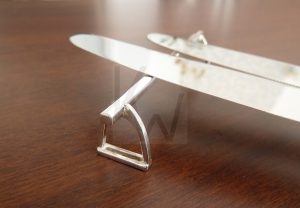 Apoyacuchillos artesanal realizado en Plata de Ley 925 con terminación pulida de alto brillo; el diseño consta de una barra central de corte cuadrado soportada lateralmente por dos figuras detalladas en forma de estribos. Una pieza de mesa sofisticada que combina la geometría limpia de su estructura con la tradición hípica, garantizando estabilidad y distinción en la presentación de la cubertería.