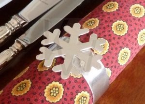 Aro de servilleta artesanal en Plata de Ley 925 que presenta un gran copo de nieve detallado montado sobre la estructura circular; la pieza se muestra con un elegante acabado satinado, aunque permite la personalización con otras terminaciones como pulido brillo, martillado o estampado, adaptándose al estilo de cada celebración.