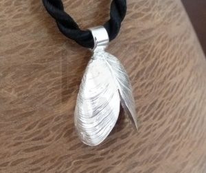 Colgante artesanal de plata con la forma de un mejillón abierto, con detalles realistas en la textura de la concha y un acabado pulido en los bordes, presentado sobre un cordón negro liso.