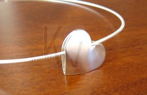 Colgante de diseño artesanal realizado en Plata de Ley 925 compuesto por dos corazones de gran tamaño y forma convexa, soldados entre sí para crear una estructura sólida y armoniosa; la pieza presenta un acabado pulido de alto brillo y se desliza con elegancia a través de una cadena rígida tipo omega, la cual recorre el espacio natural formado por la unión de ambos corazones.