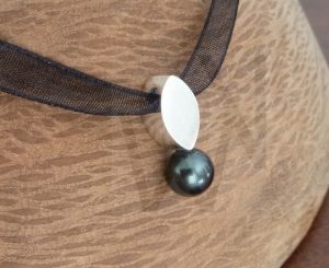 Colgante artesanal de diseño orgánico realizado en plata, con una perla de Tahití de tonos oscuros suspendido de una hoja estilizada, presentado sobre un cordón de seda que resalta la elegancia natural de la gema.