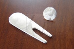 Accesorio de golf artesanal compuesto por un arreglapique masivo de plata y marcapelotas; la superficie de la pieza presenta un acabado texturizado que imita la escarcha de la mañana y el agua congelada sobre la Plata de Ley 925, logrando un diseño robusto a la vez que elegante.