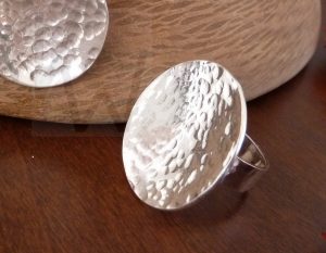 Anillo artesanal de plata con diseño circular ligeramente cóncavo y superficie con textura martillada que evoca el movimiento del agua, montado sobre una banda de plata que mantiene el estilo minimalista y orgánico de la colección.