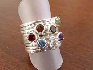 Conjunto artesanal de nueve anillos individuales de plata; siete de ellos cuentan con una piedra semipreciosa de 4 mm (topacio, granate, amatista, citrino, peridoto, cuarzo ahumado y cuarzo blanco), enmarcados por dos anillos de plata lisa en los extremos para un diseño equilibrado y armónico.