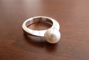 Anillo artesanal forjado en Plata de Ley 925 con un diseño escultórico de perfil triangular; la estructura se eleva y se expande en la parte superior para crear un espacio preciso donde se aloja una perla natural. La técnica de forjado permite que la gema parezca estar suspendida en el aire, sostenida únicamente por la tensión y la forma del metal pulido.