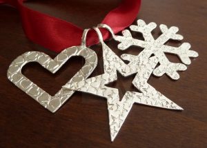 Trío de adornos navideños en Plata de Ley 925 compuesto por una estrella, un corazón y un copo de nieve con motivos estampados y acabado pulido, presentados sobre un lazo rojo.