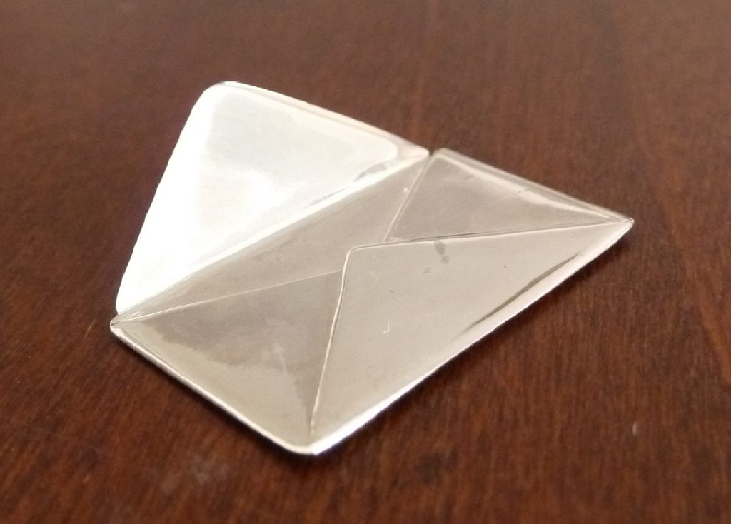 Objeto artesanal en forma de sobre realizado en plata de ley con acabado pulido espejo, simbolizando la comunicación y el contacto personal con el autor.